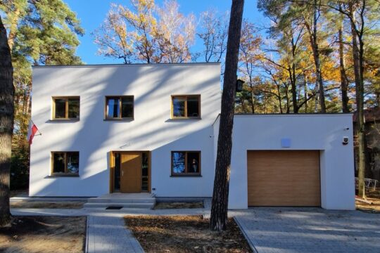 Drewniany dom modułowy Simple House z prostym dachem i z garażem, na środku pień drzewa