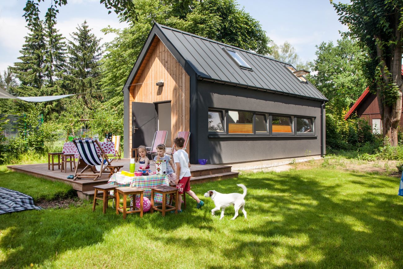 Nowoczesny dom prefabrykowany Simple House z dużym ogrodem, tarasem i rodziną spędzającą czas na świeżym powietrzu.