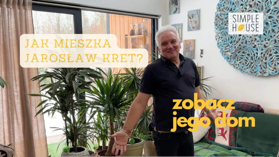 Jarosław Kret stoi w nowoczesnym salonie pełnym roślin, przy dużym oknie, prezentując wnętrze domu Simple House z napisem „Jak mieszka Jarosław Kret? Zobacz jego dom”.