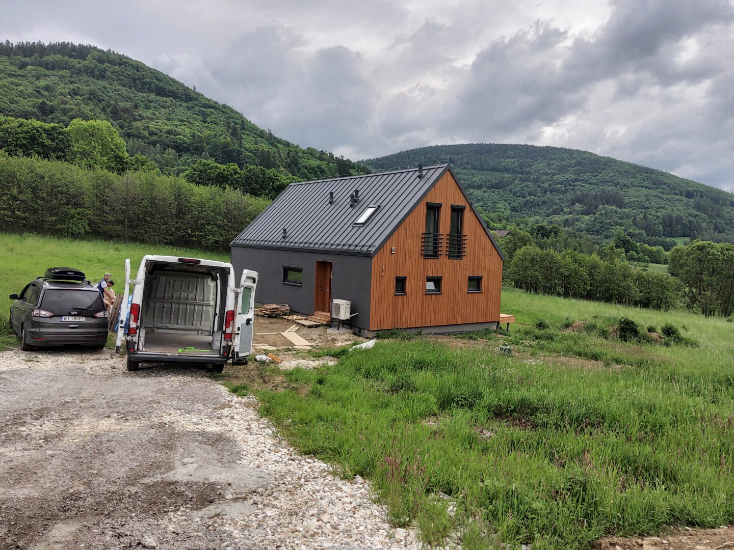 Drewniany dom modułowy Simple House na tle zielonych gór. Antracytowy dach.